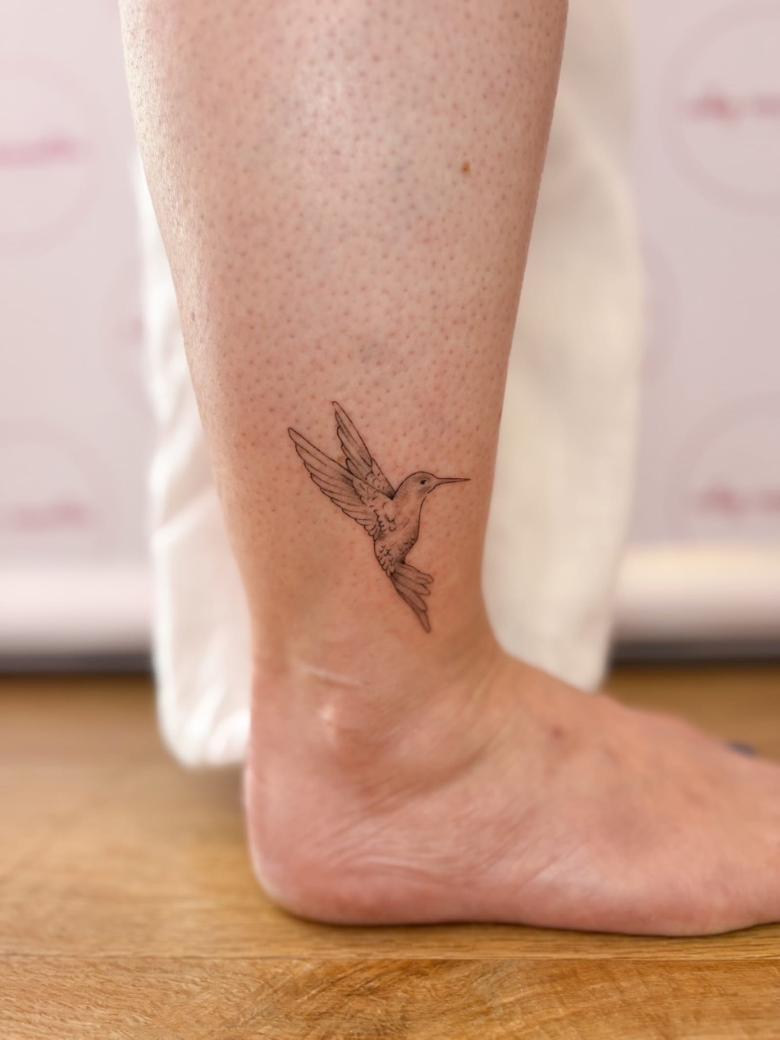 Small fine line hummingbird tattoo above the ankle
