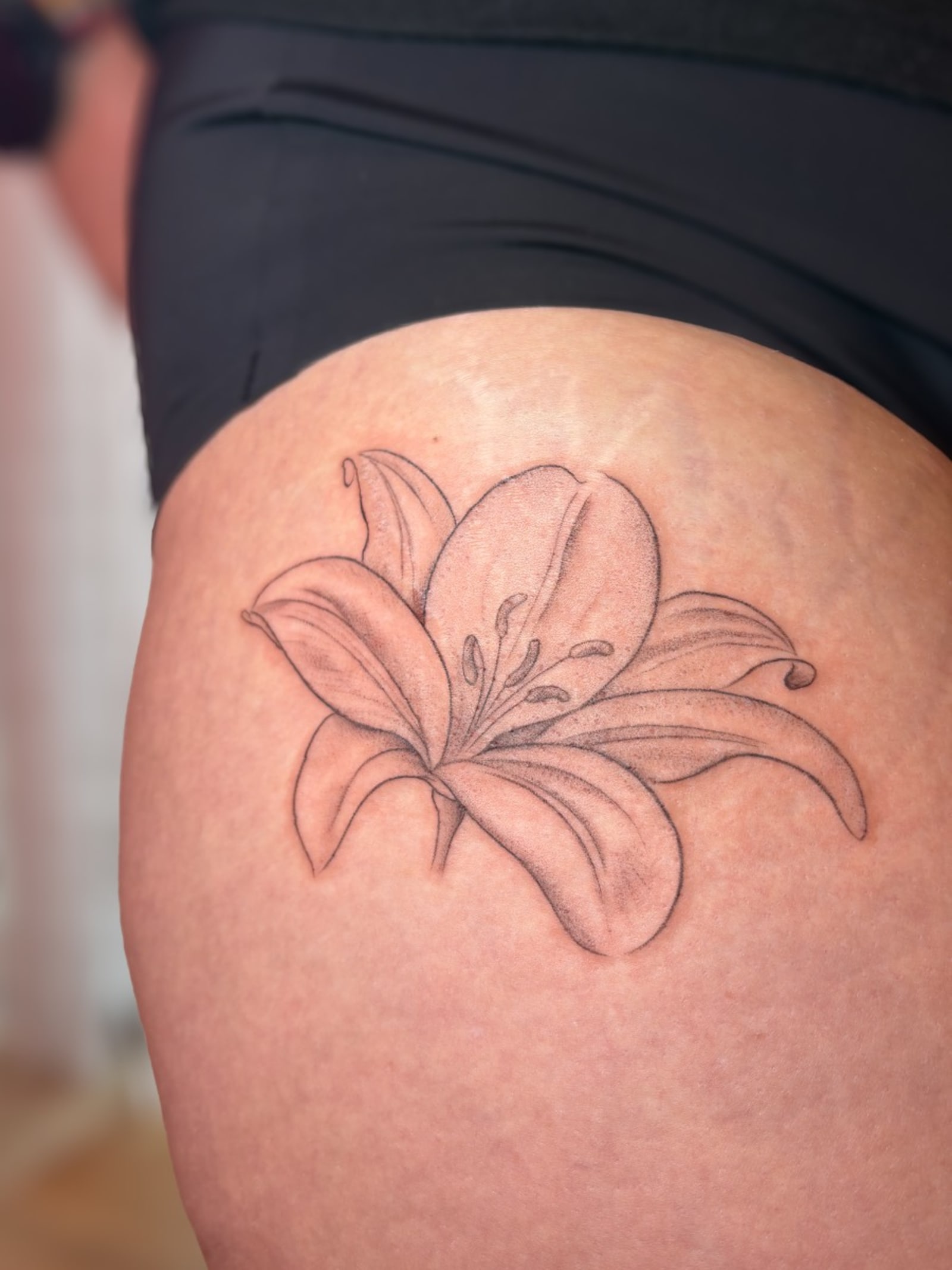 Fine line lily tattoo with softly shaded petals on a hip